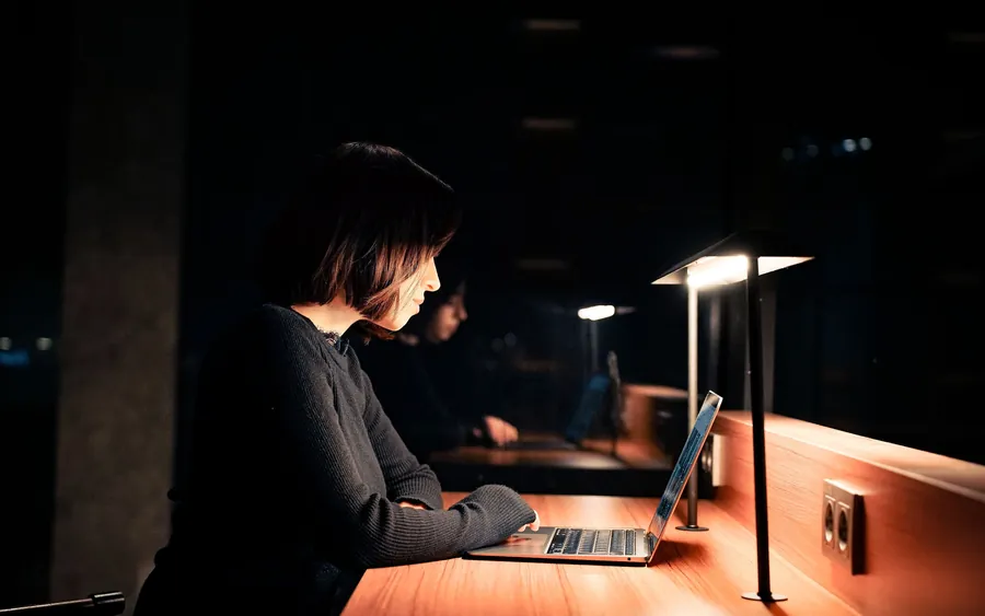 A person working alone at a lit desk in a dark office at night.